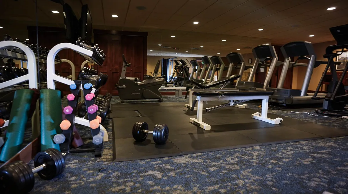 This interior image showcases a spacious fitness center equipped with treadmills, dumbbells, and a weight bench. The scene conveys an active, motivating environment ideal for wellness breaks during a workday.