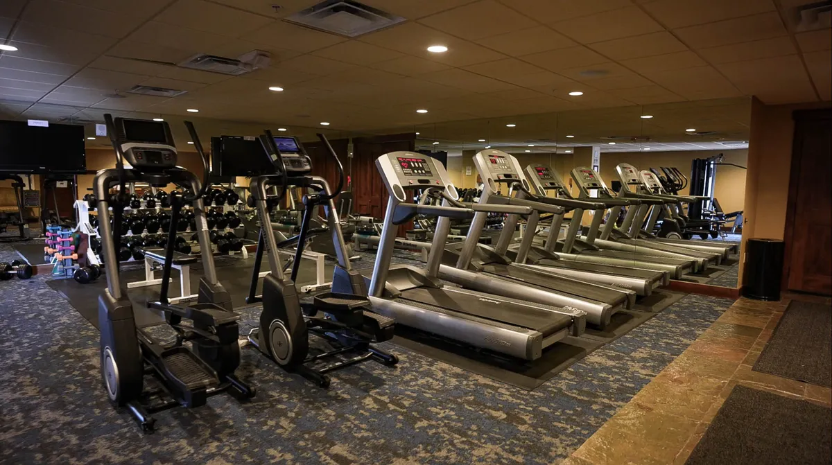 A bright and modern fitness center featuring elliptical machines, treadmills, dumbbells, and mirrored walls. The open layout and plentiful equipment invite guests to pursue their wellness routines in a motivating environment.