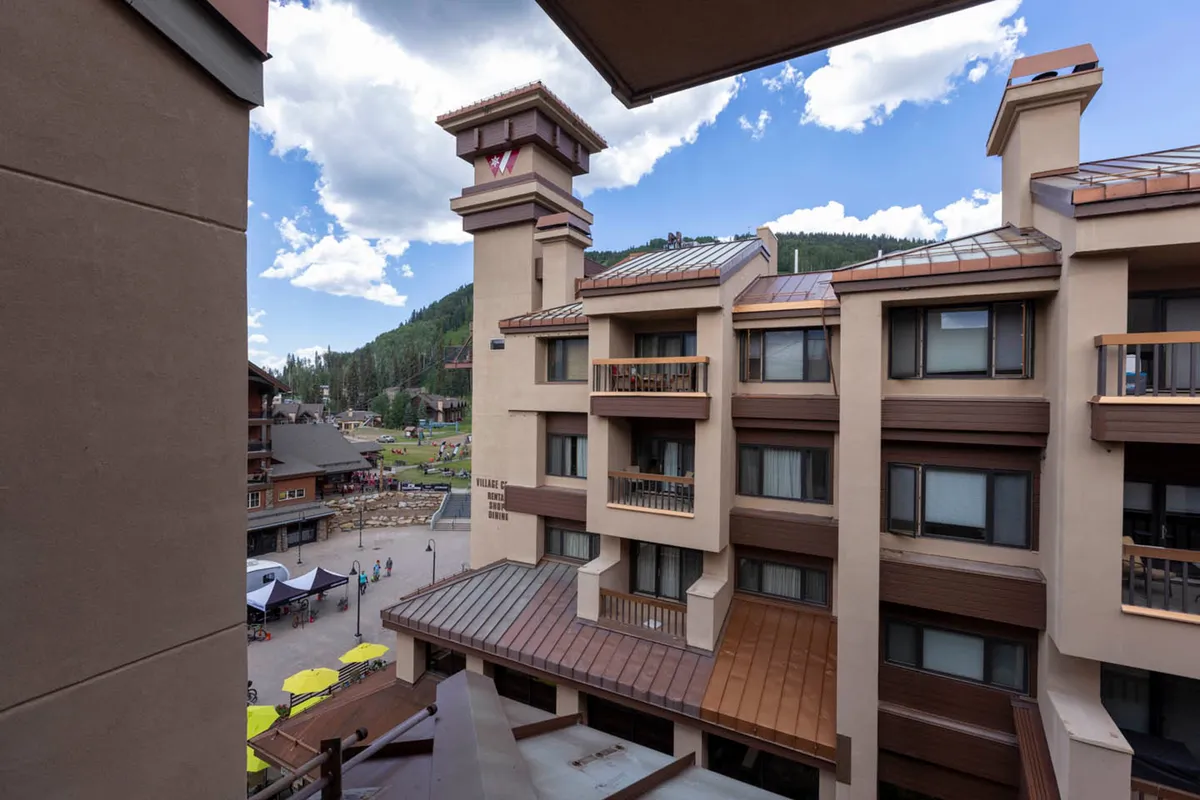 This image features the vibrant heart of the resort village, with the striking mountain backdrop, attractive building facades, and multiple balconies with seating. The outdoor gathering area below is lively, suggesting a setting perfect for socializing, relaxing, and participating in local events or festivals.