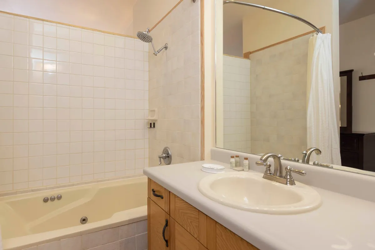 A modern, inviting bathroom featuring a spacious bathtub, a sleek sink and mirror, a glass-enclosed shower, and warm wooden cabinetry. The space exudes calm with its clean lines and soothing palette, ideal for relaxation and self-care routines.