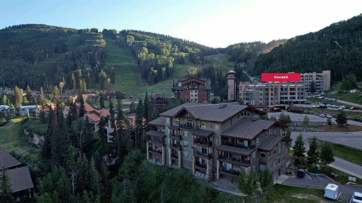 A tranquil resort exterior framed by dramatic mountain scenery, wooden architecture, and green pine trees. The scene evokes a sense of both relaxation and adventure, with hints of skiing, hiking, and outdoor dining available within the resort environment.