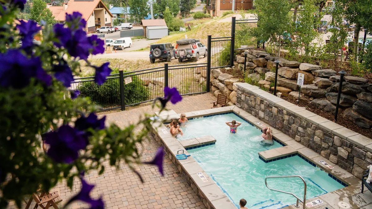 This image features a sparkling outdoor swimming pool surrounded by flowers and a comfortable seating area. The pool is inviting, with sunset light creating a warm, relaxing atmosphere. It hints at the perfect way to unwind after a day on the slopes or trails, connecting relaxation and recovery closely to the adventure experience.