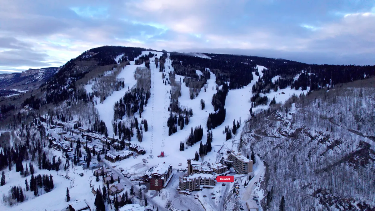A panoramic view of snow-covered ski slopes, residential buildings nestled among trees, and majestic mountains under an expansive sky. The scene radiates a sense of adventure and natural beauty, highlighting the picturesque surroundings and year-round activities available right outside the retreat.