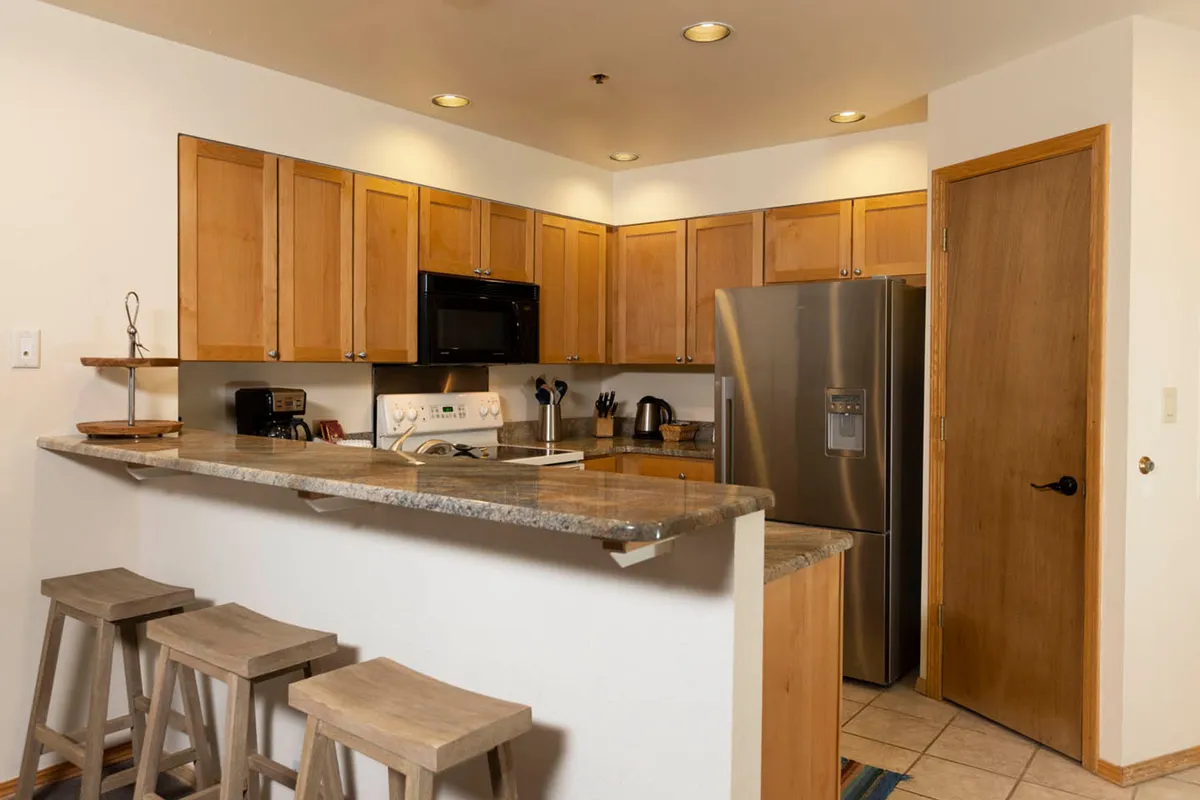 This image focuses on the kitchen itself, showcasing granite countertops, stainless steel appliances, and warm wooden cabinetry. The arrangement is perfect for meal prep and socializing while cooking.