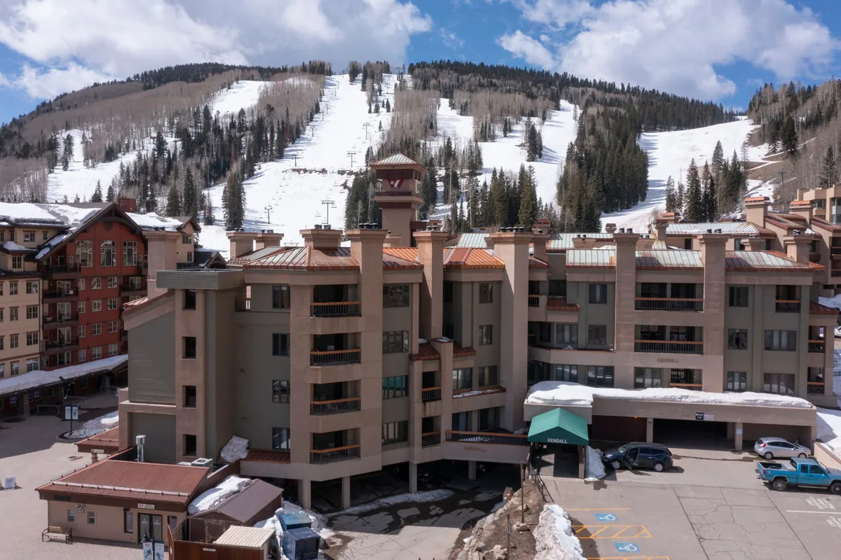 This image shows the exterior of the resort with a snow-covered mountain backdrop, modern architecture, and hints of the surrounding forest. The scene is lively and inviting, with clear sightlines to the ski slopes and easy access points to outdoor adventures such as skiing, snowboarding, and hiking. The image evokes the resort as a basecamp for mountain activities, with the building nestled comfortably in a dramatic alpine setting.